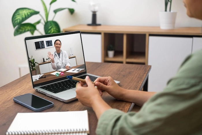 Person having a telehealth virtual medical consultation on a laptop, speaking with a doctor on a video call.